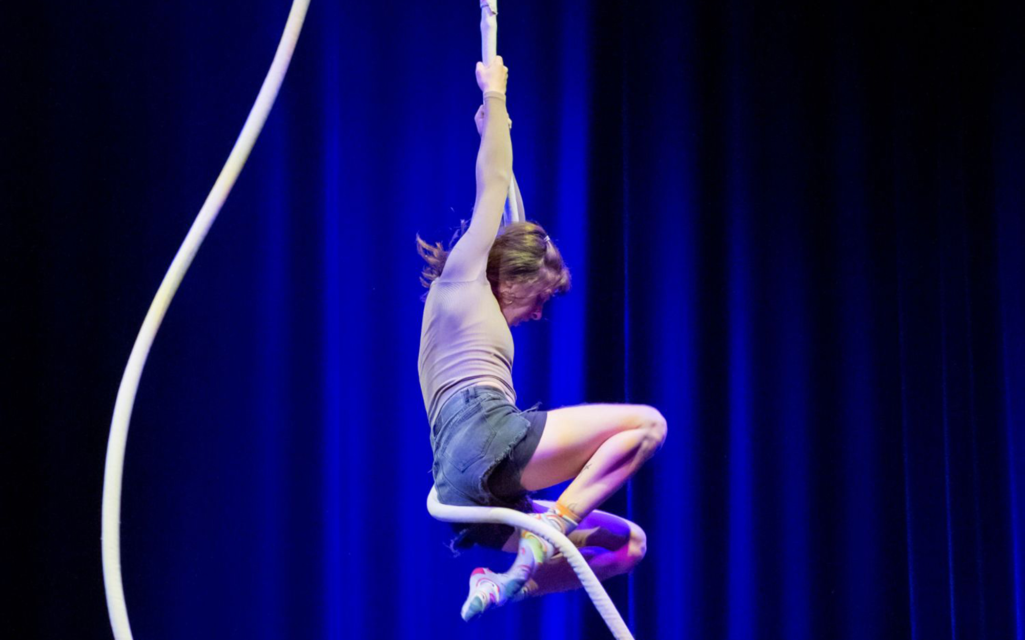 Aerial rope artists performs at Circomedia in front of a blue background. Two ropes dangle from the ceiling.